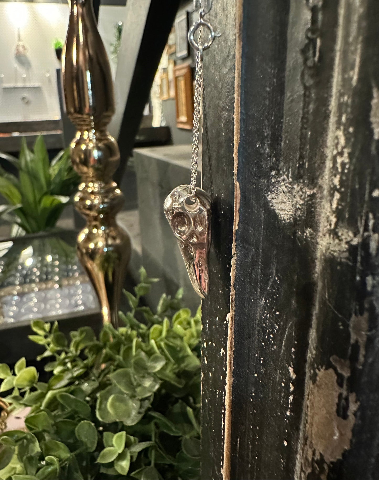 Silver bird skull against decorative gold candlestick with a mirror and greenery in the background