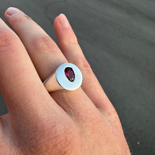Close-up of a hand wearing a signet ring with a red gemstone on a dark background