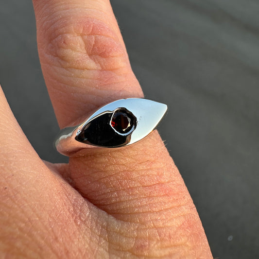 Silver ring with a red gemstone on a finger against a dark background