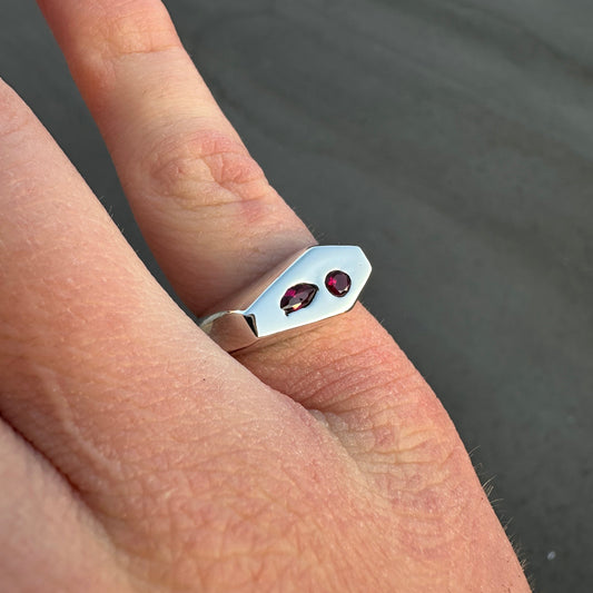 Silver ring with red gemstones on a finger against a dark background